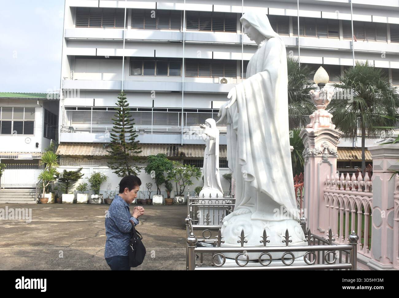 Donna asiatica anziana in piedi e rispettare di fronte alla chiesa di Santa Cruz antica comunità di portoghese cristiano luogo di viaggio in Thailandia Foto Stock