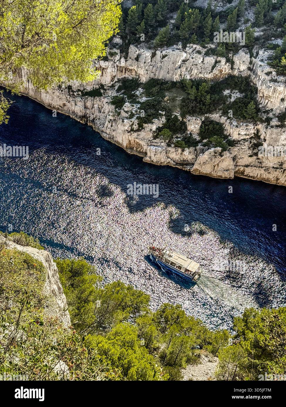 Tour in barca navigando in acque cristalline e profonde, circondate da alte scogliere e pini verdi Foto Stock