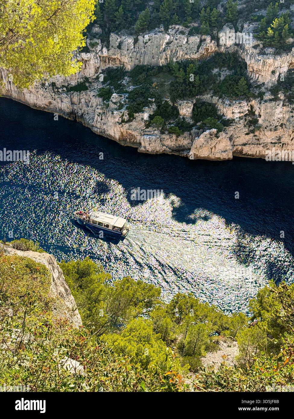 Barca da diporto che naviga in acqua frizzante in una stretta insenatura delimitata da impressionanti scogliere Foto Stock