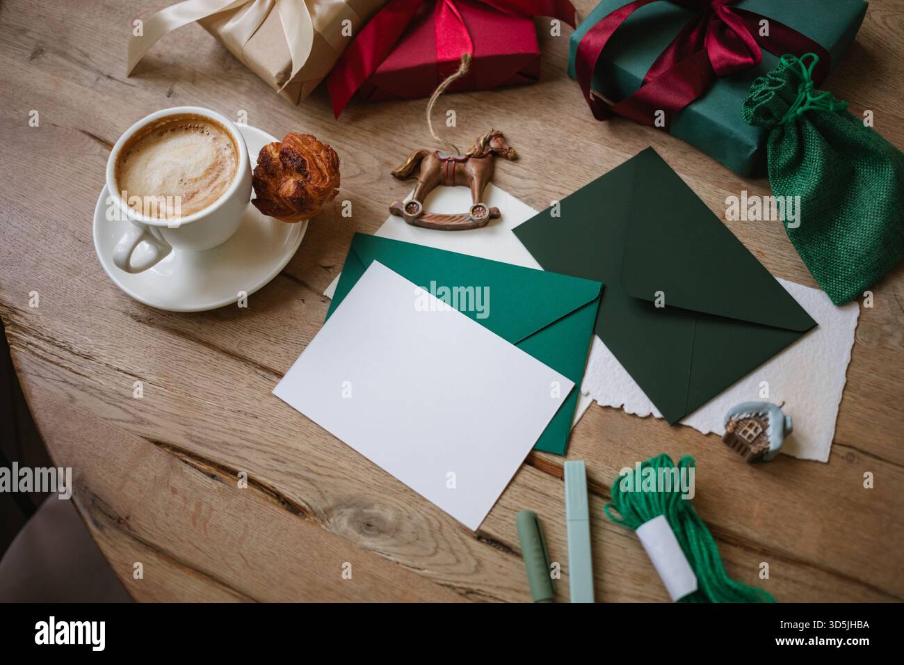 Vista dall'alto di un cappuccino su un tavolo con un biglietto bianco, regali di Natale avvolti e decorazioni natalizie assortite Foto Stock