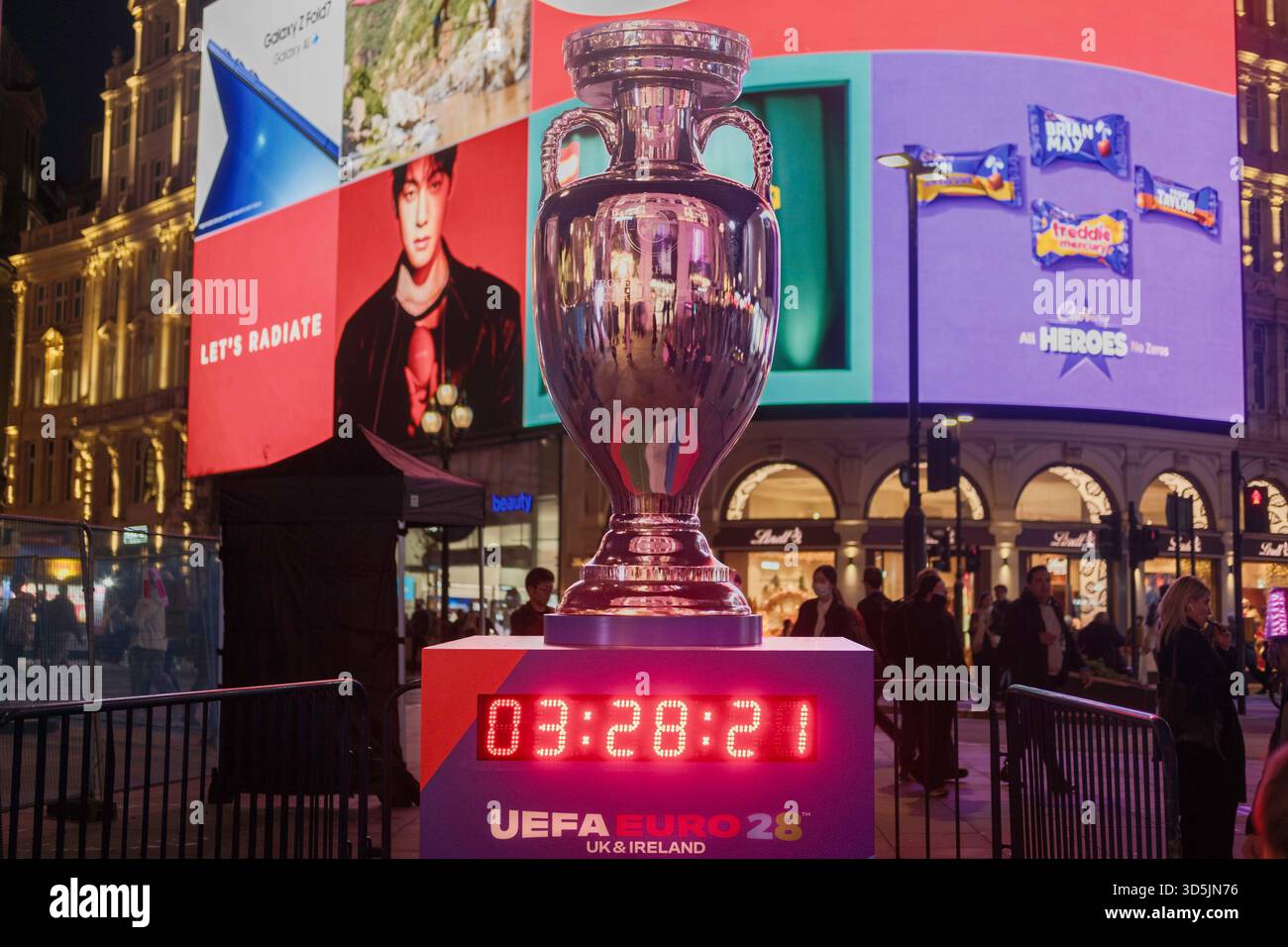 Londra, Regno Unito. 12 novembre 2025. Il torneo di calcio UEFA EURO 2028 che si terrà nel Regno Unito e in Irlanda è ufficialmente lanciato a Londra. Nella foto: Una replica del trofeo Henri Delaunay UEFA Euro Championship è esposta a Piccadilly Circus sopra un conto alla rovescia per l'inizio dei campionati a Cardiff il 9 giugno 2028. Foto Stock