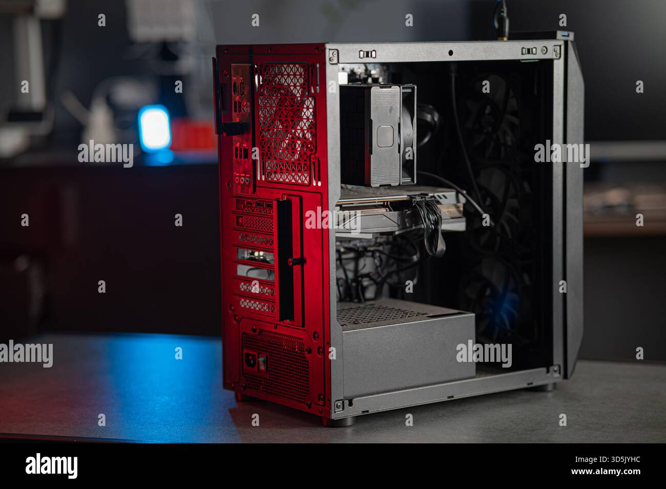 telaio del pc desktop aperto che mostra la scheda madre illuminata da un'illuminazione d'accento rossa, interni esposti con alimentatore, ventola di raffreddamento, cavi e alloggiamenti per unità accesi Foto Stock