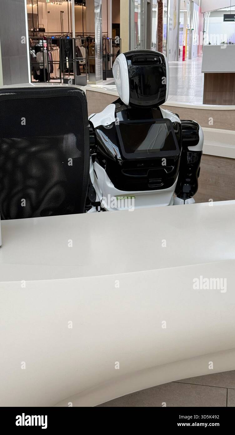 Receptionist robot in un moderno ambiente di vendita al dettaglio con bancone bianco e attrezzature high-tech. Foto mobile Foto Stock