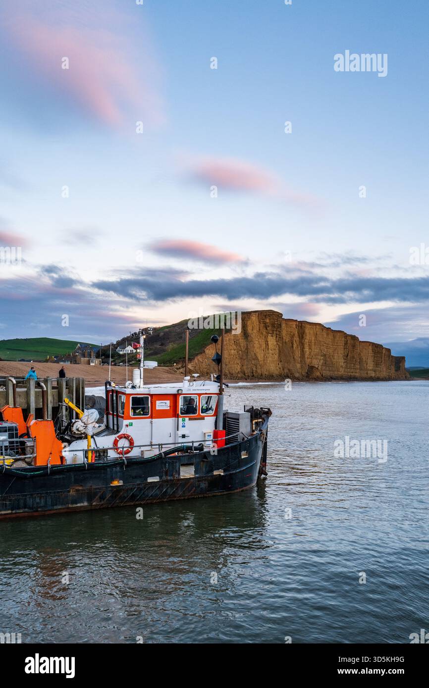 Nave da dragaggio nel porto di West Bay al tramonto che elimina il limo dal porto usando acqua pressurizzata. Foto Stock