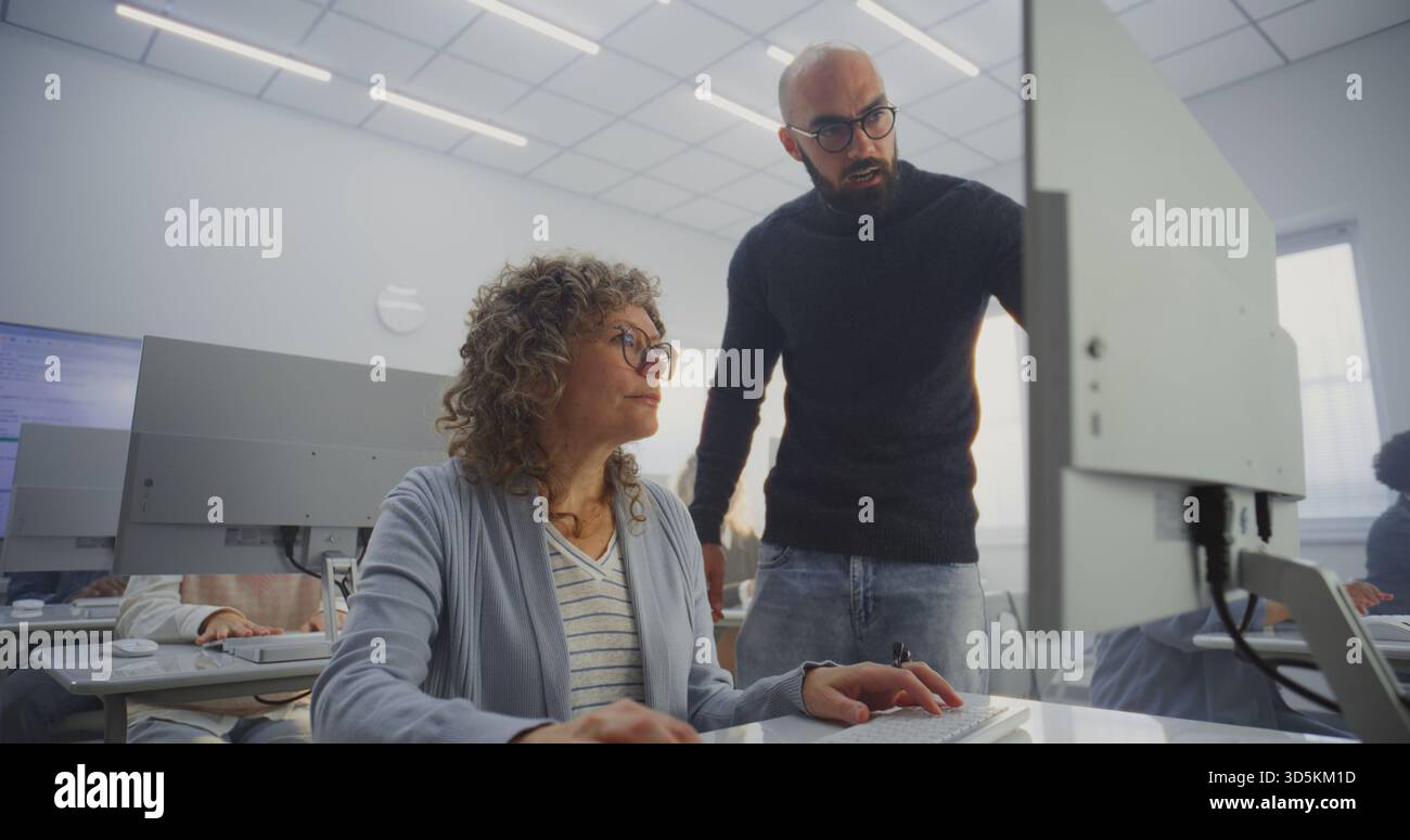 Diversi studenti maturi esercitano le competenze digitali sotto la supervisione di insegnanti maschi in Bright computer Class. Inclusione dei concetti, miglioramento delle competenze, apprendimento continuo e potenziamento digitale. Angolo alto. Foto Stock