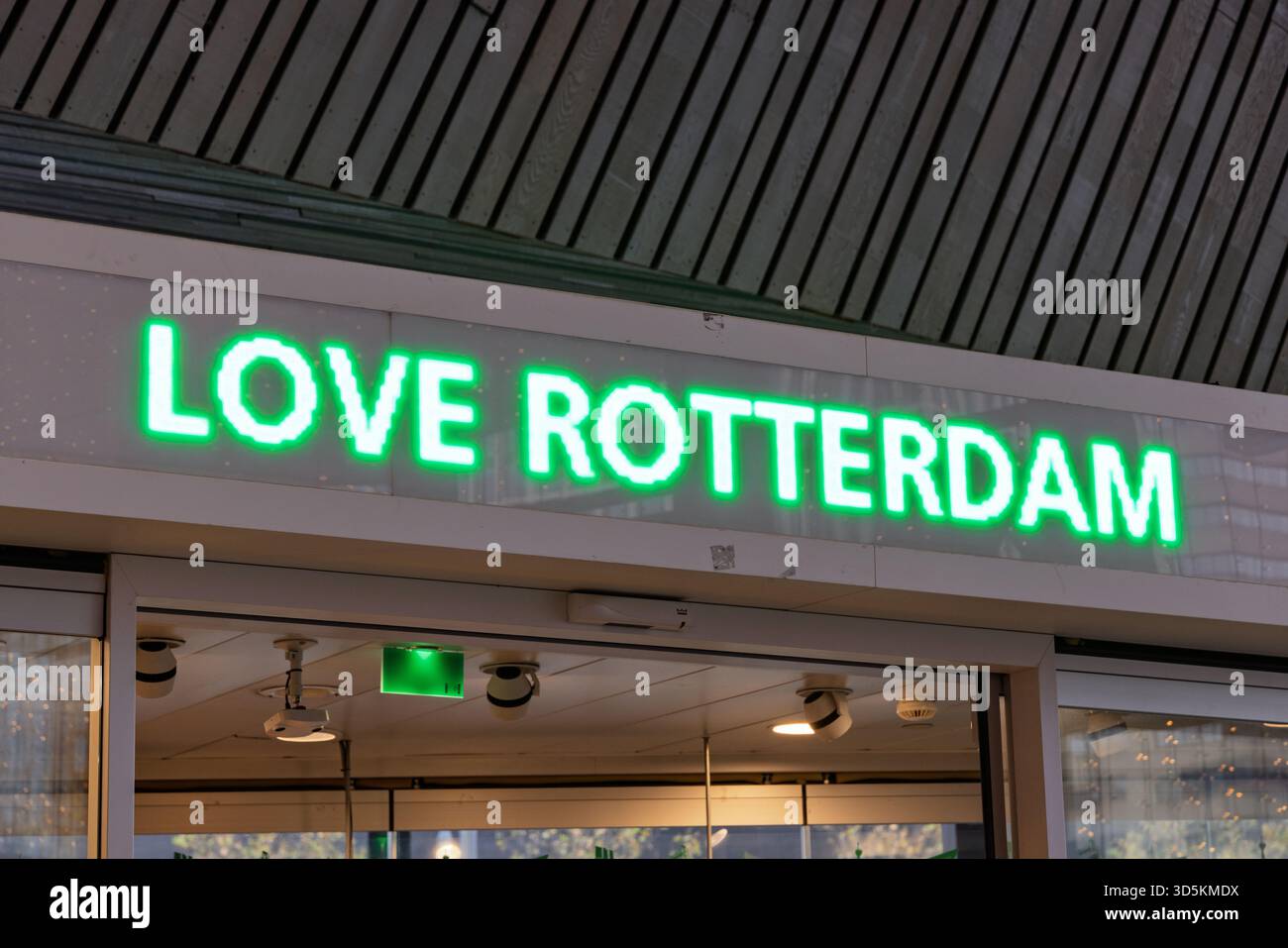 Un cartello LED verde luminoso che mostra "LOVE ROTTERDAM" sopra un'entrata, adagiato su una moderna struttura a soffitto in un centro cittadino olandese. Rotterdam Foto Stock