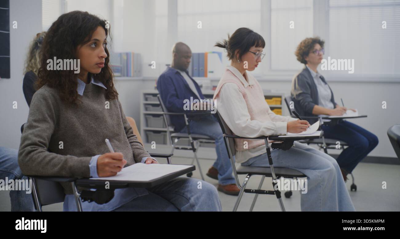 Diversi studenti adulti si sono concentrati sull'attività di scrittura durante la lezione in aula. Concetto di ambiente di apprendimento moderno che promuove l'inclusione, la crescita delle competenze e il progresso educativo. Colpo di Dolly. Foto Stock