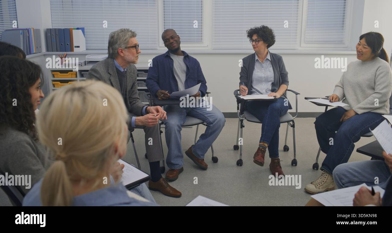 Gli studenti maturi si siedono nel Discussion Circle, interagendo con l'istruttore in uno spazio di apprendimento calmo e ben illuminato. Concetto di attenzione e coinvolgimento, ambiente educativo professionale ma rilassato. Foto Stock