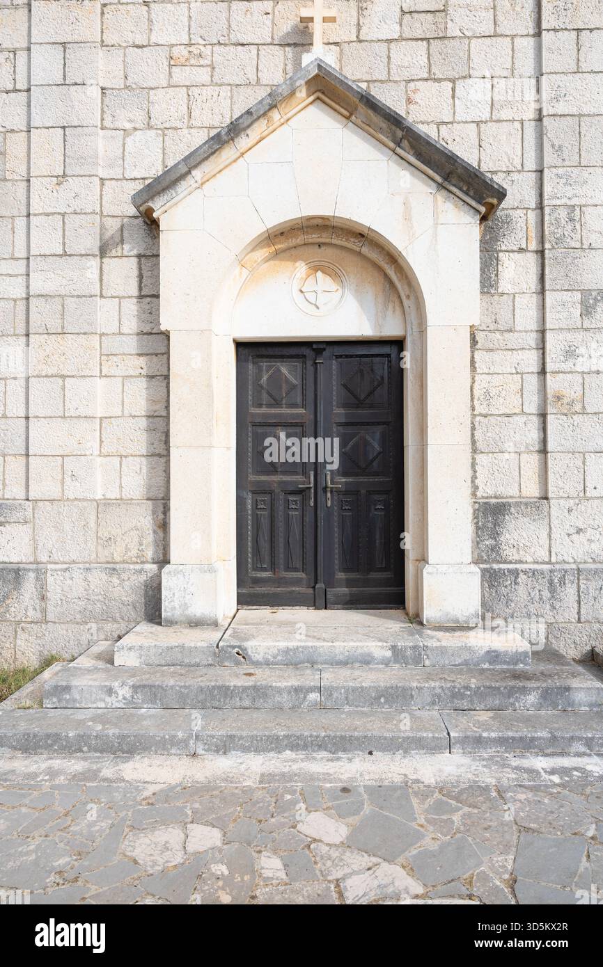 Una chiesa di pietra intemprata. Porte verdi e muratura rustica evocano un'architettura rurale senza tempo e una fede tranquilla. Foto Stock