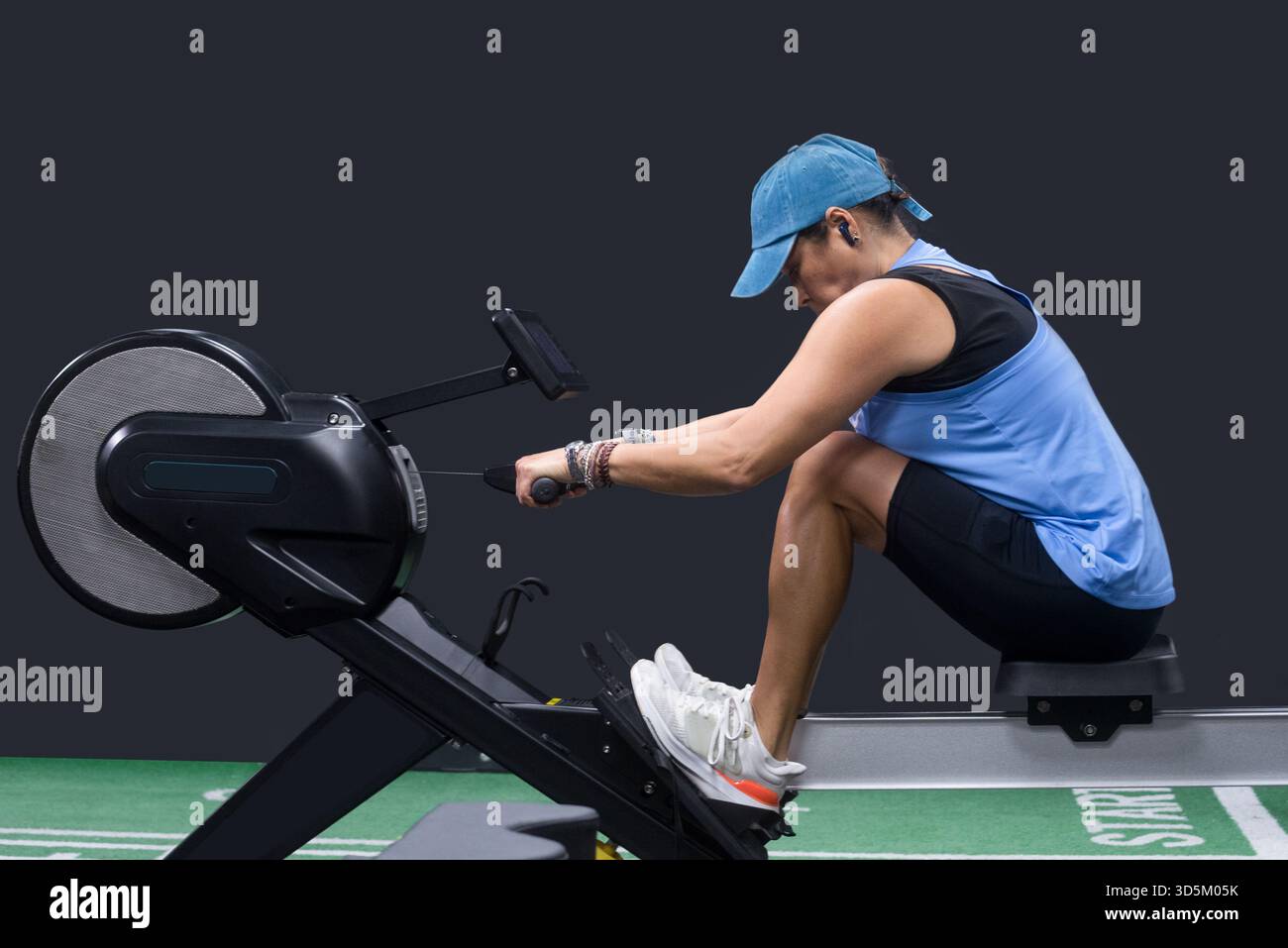 Una donna di mezza età che si allena su un vogatore, indossa un berretto e un abbigliamento sportivo blu. Foto Stock