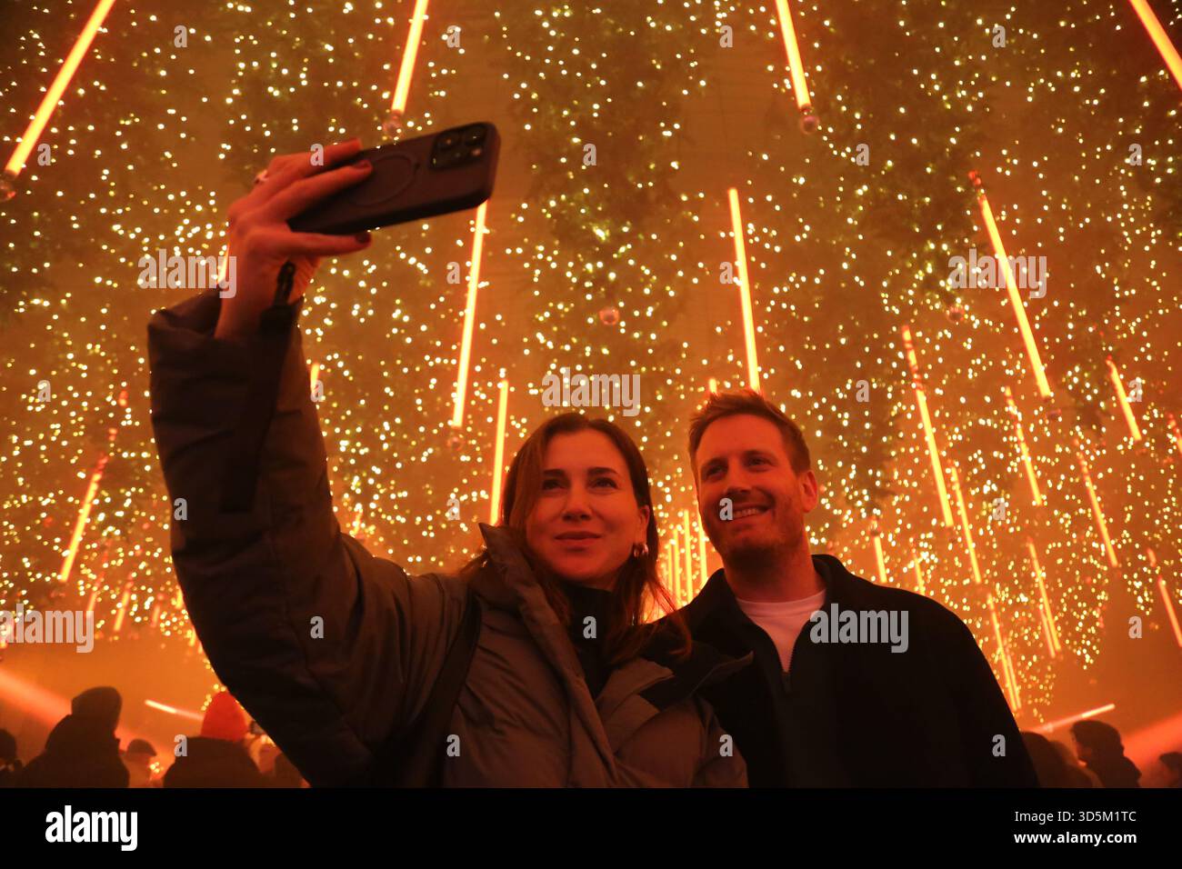 Berlino, Germania. 15 novembre 2025. Una coppia scatta un selfie accanto a una pista di pattinaggio presso l'installazione artistica Dark Matter: Forest Winterlights 2025, creata dall'artista tedesco Christopher Bauder al Dark Matter Light and Media Art Museum di Berlino. L'installazione si estende su una superficie di 1.000 metri quadrati e dispone di oltre 600 alberi galleggianti e 250.000 luci, il tutto su una composizione del musicista olandese Chris Kuijten. L'esperienza combina l'esposizione visiva con l'opportunità di pattinare su una pista di pattinaggio integrata nell'installazione. (Credit Image: © Rouzbeh Fouladi/ZUMA Press Wire) EDITORIALE USA Foto Stock
