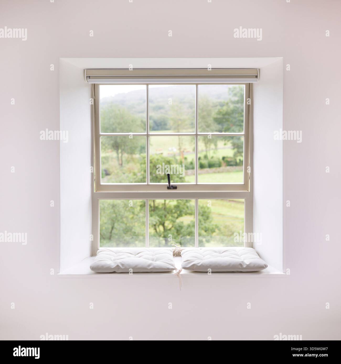 Tradizionale finestra a telaio in legno con un sedile imbottito, adagiata su pareti bianche in una casa del Regno Unito, con una vista panoramica della campagna Foto Stock