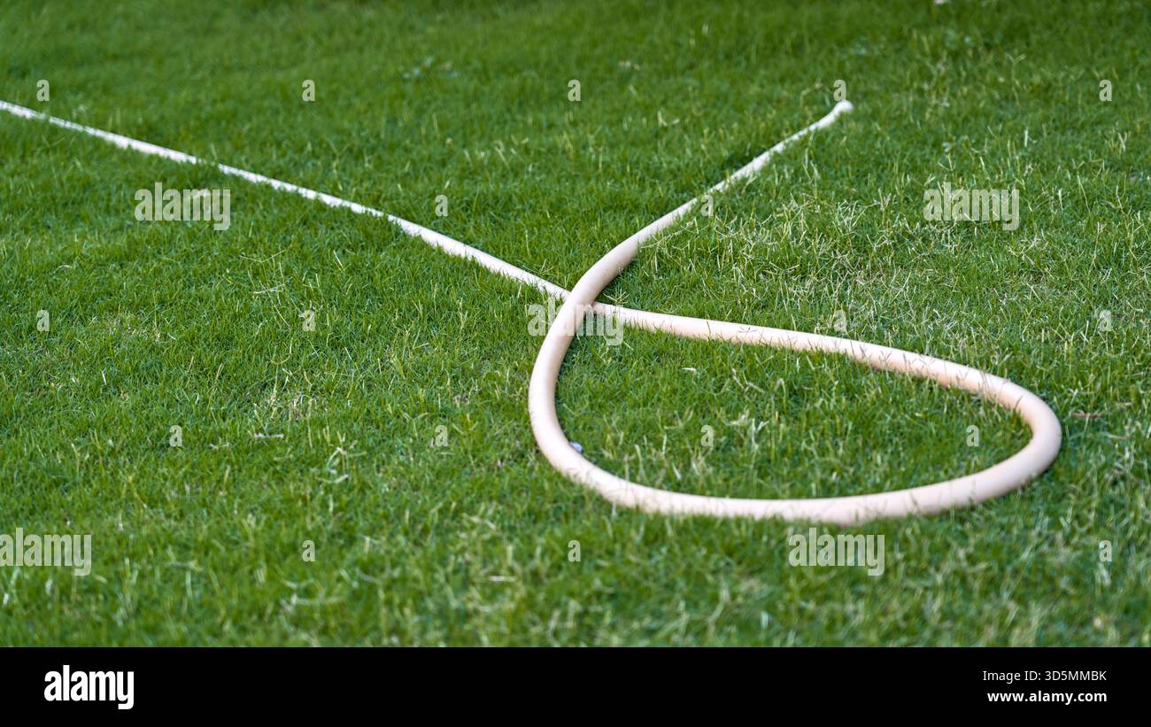Un tubo da giardino beige leggero si trova su un prato ben curato, aggiungendo un tocco semplice e naturale all'ambiente esterno. Foto Stock