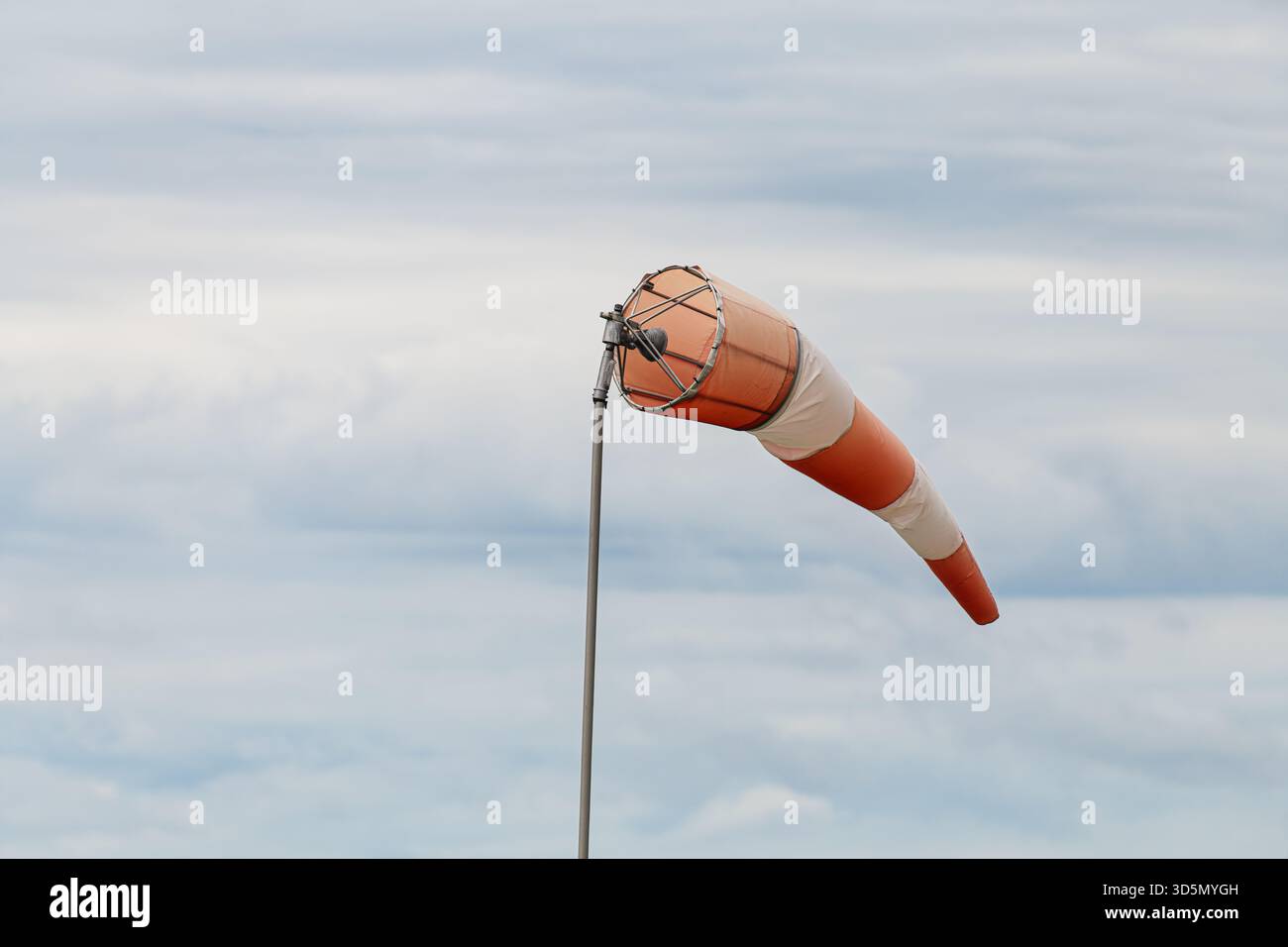Calza a vento a righe arancioni e bianche su asta in metallo estesa orizzontalmente dal vento contro il cielo grigio nuvoloso. Ripresa a livello degli occhi con indicazione della direzione del vento Foto Stock