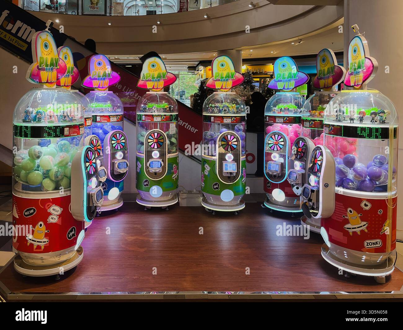 Balikpapan, Indonesia - 16 novembre 2025. Una fila di distributori automatici di artigli illuminati con temi alieni o UFO luminosi e capsule premio colorate o b Foto Stock