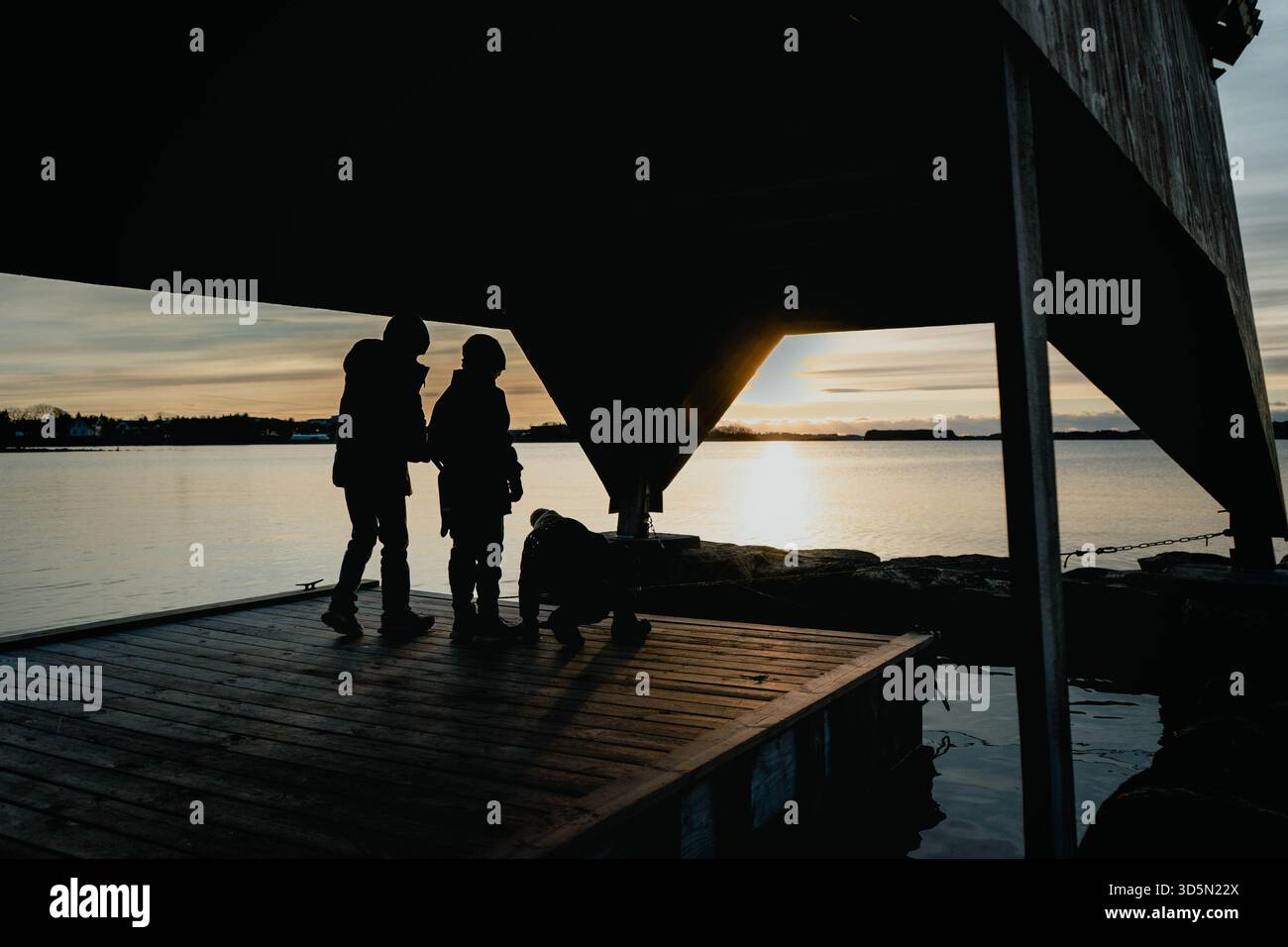 I bambini esplorano un molo costiero al tramonto, una silhouette spettacolare e la luce dell'ora d'oro. Foto Stock