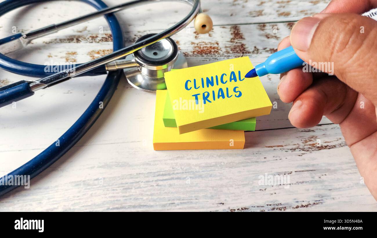 Scrittura a mano "Clinical Trials" su una pila di note adesive accanto a uno stetoscopio, illustrando la ricerca medica e lo sviluppo di farmaci Foto Stock