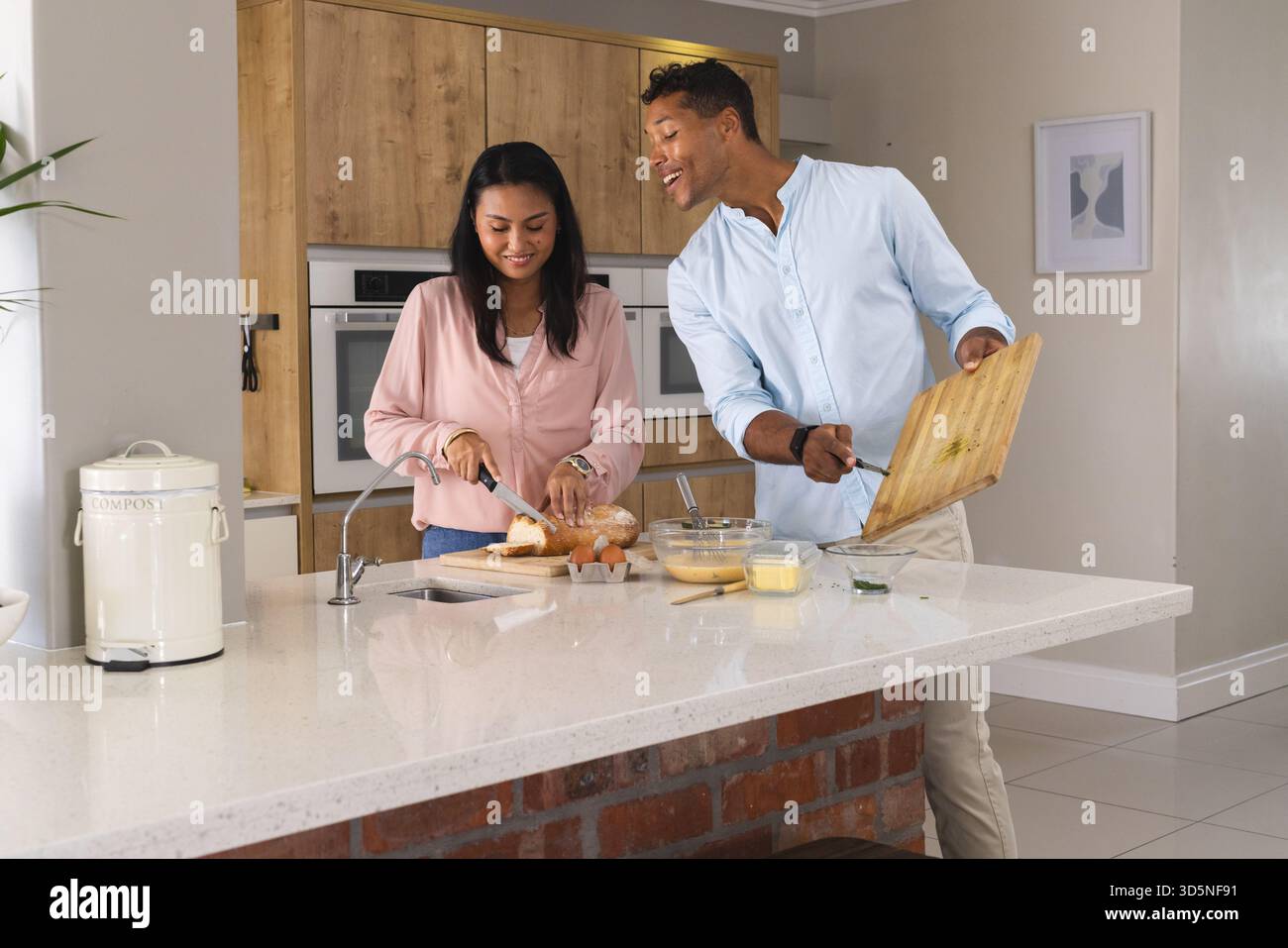 Coppia che prepara la colazione insieme in una cucina moderna, sorridendo e godendo la mattina Foto Stock