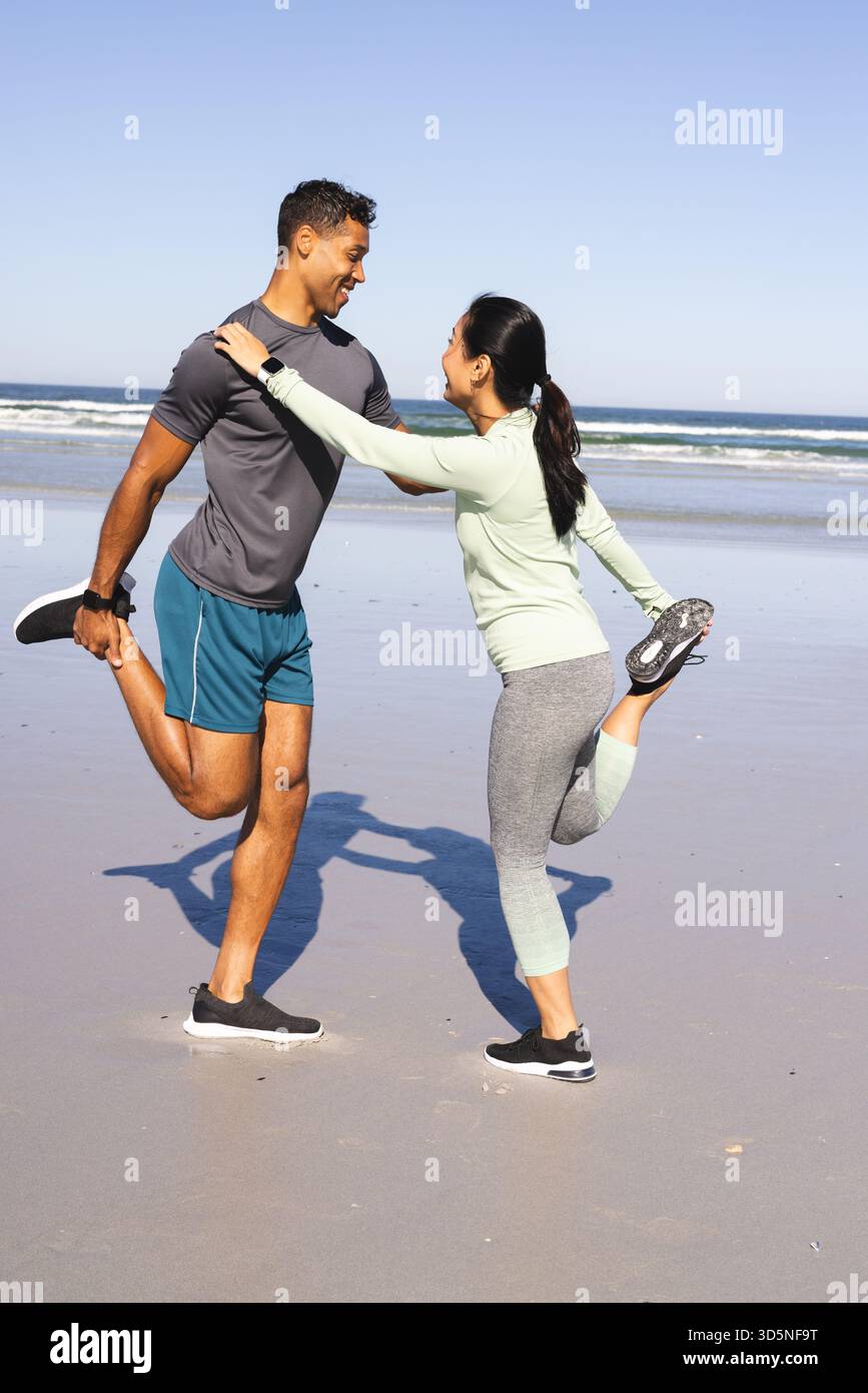 Coppia che si allunga insieme sulla spiaggia, godendosi l'esercizio mattutino vicino all'oceano Foto Stock