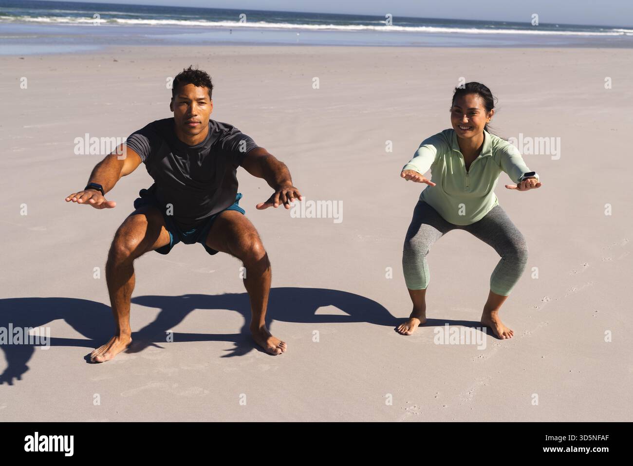 Coppia che si allenano sulla spiaggia, fanno gli squat insieme, si allenano al mattino Foto Stock