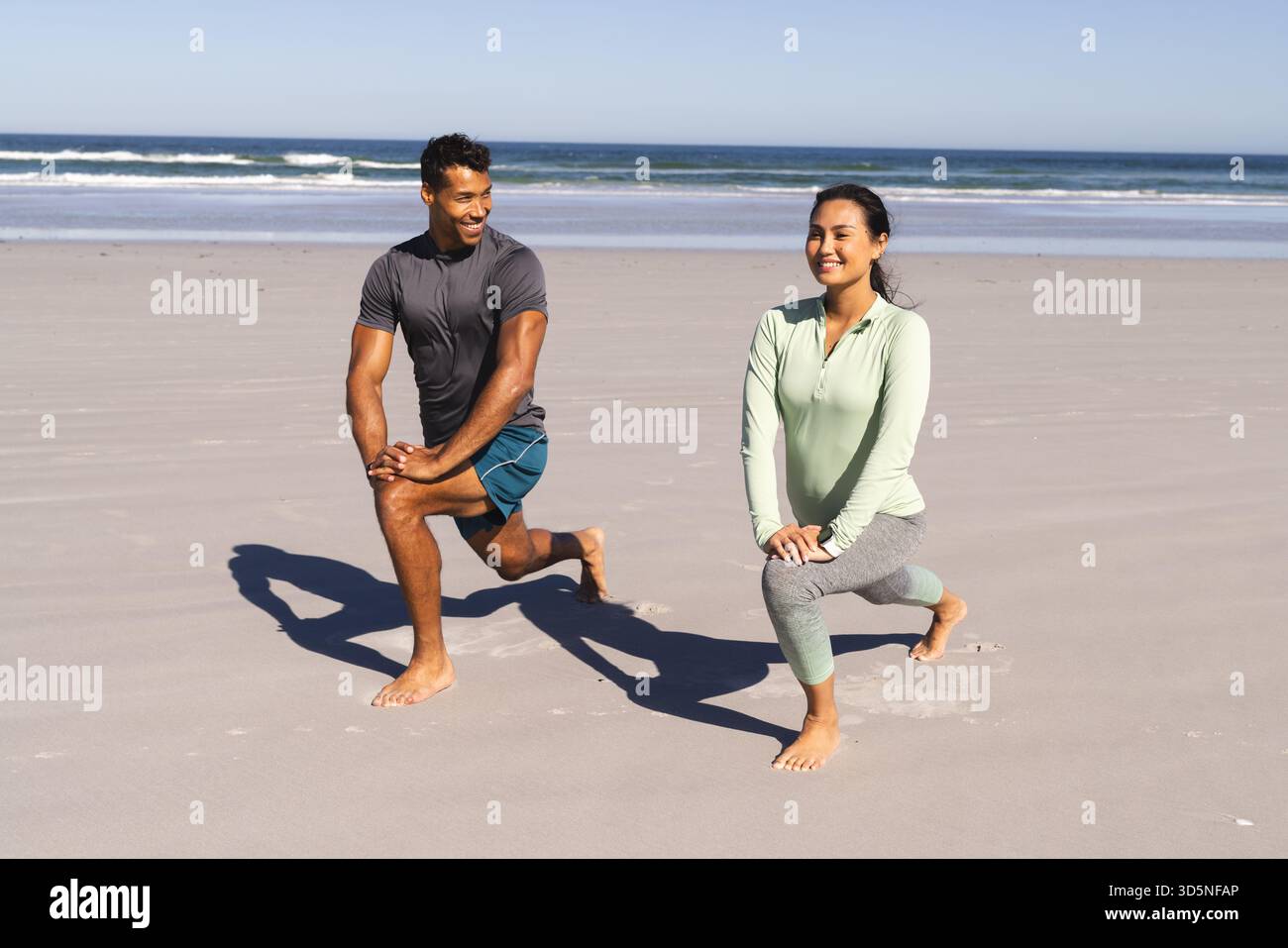 Coppia che si fa esercizio sulla spiaggia, fa affondamenti e sorride l'un l'altro Foto Stock