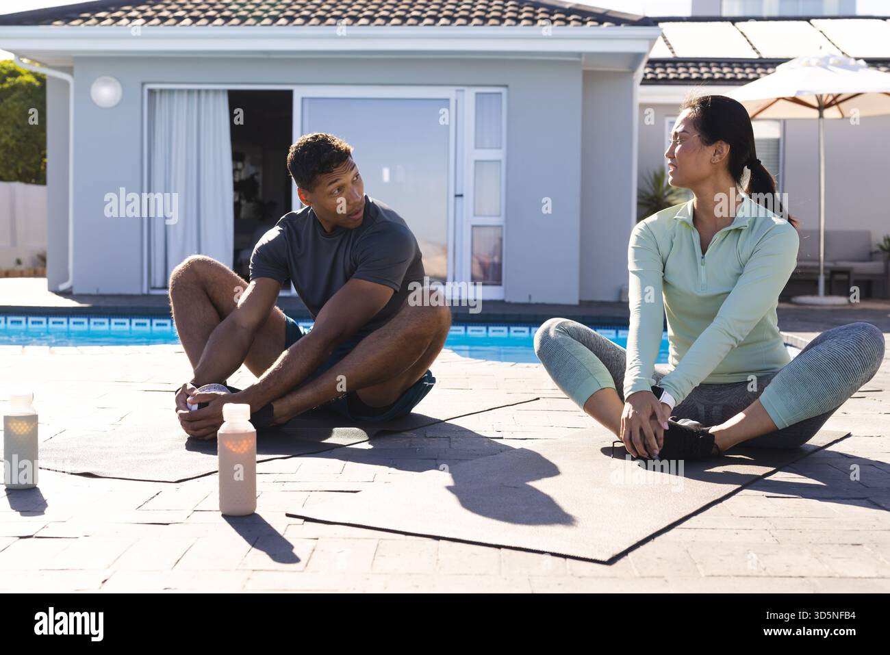Coppia che si allunga sui tappetini per lo yoga in piscina e si diverte ad allenarsi insieme al mattino Foto Stock