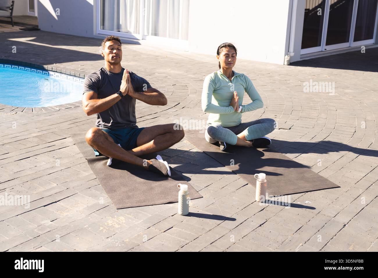 Coppie che meditano sui tappetini da yoga a bordo piscina, godendosi una tranquilla routine mattutina Foto Stock