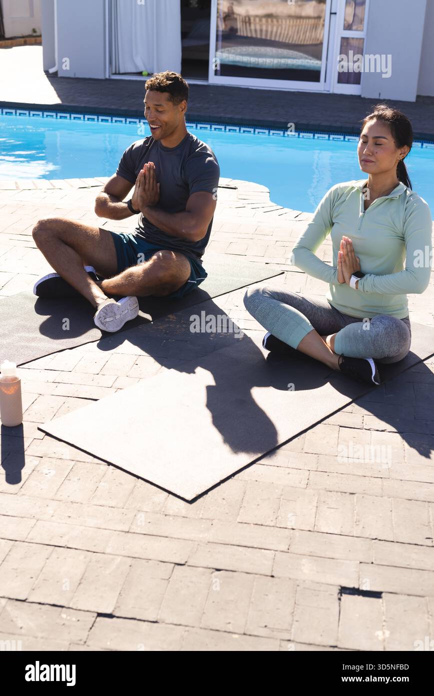 Coppie che meditano in piscina su stuoie per yoga, godendosi una tranquilla routine mattutina Foto Stock