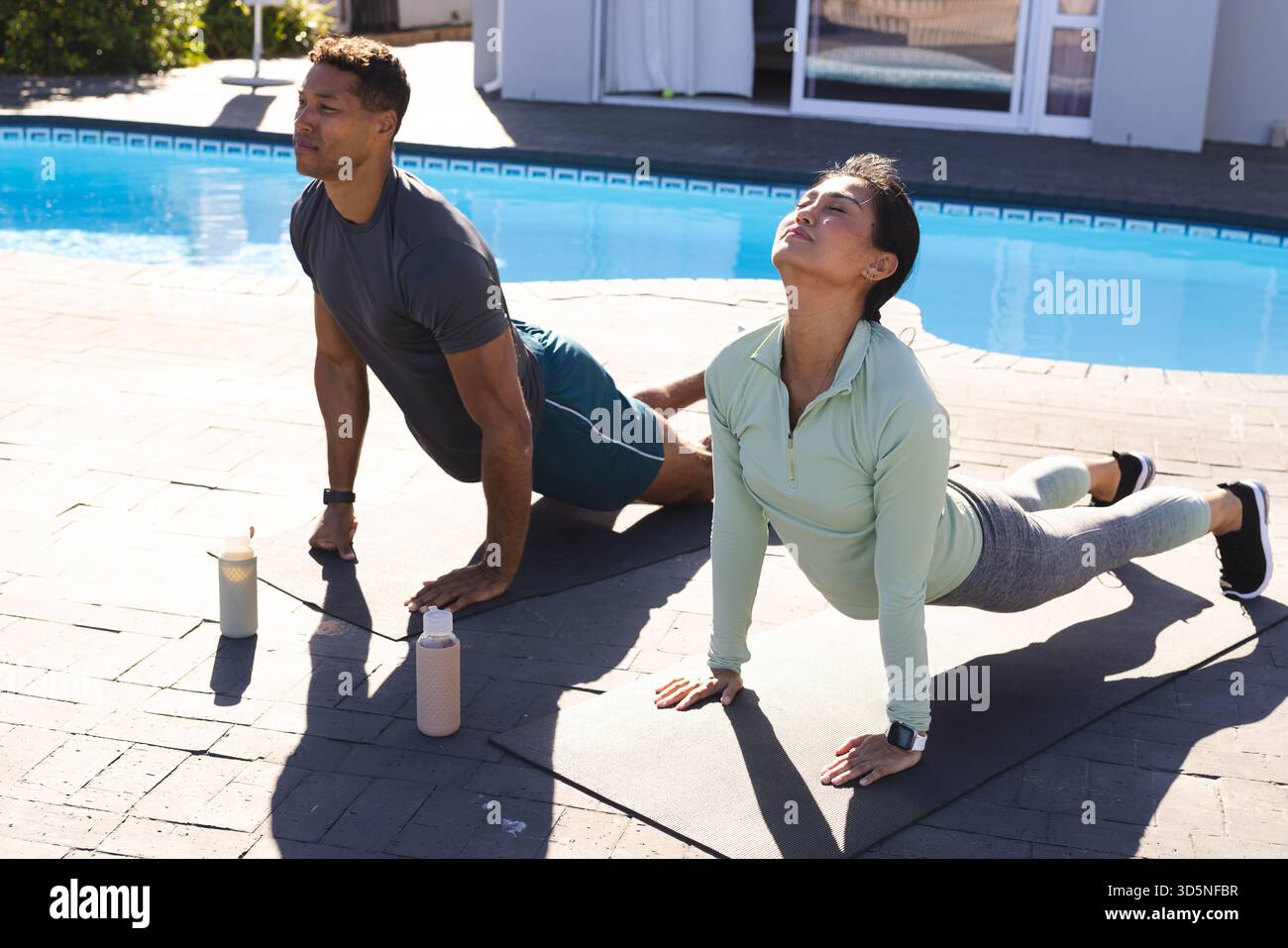 Coppia che pratica yoga in piscina, si allunga e si rilassa alla luce del sole mattutino Foto Stock
