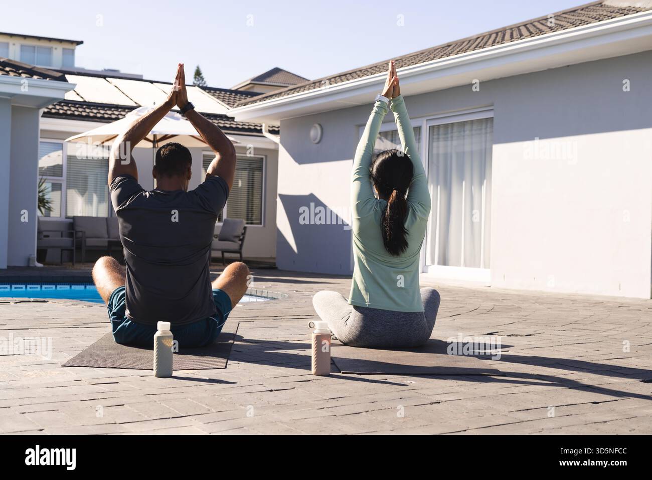 Coppie che praticano yoga all'aperto su materassini a bordo piscina e si godono gli esercizi mattutini Foto Stock