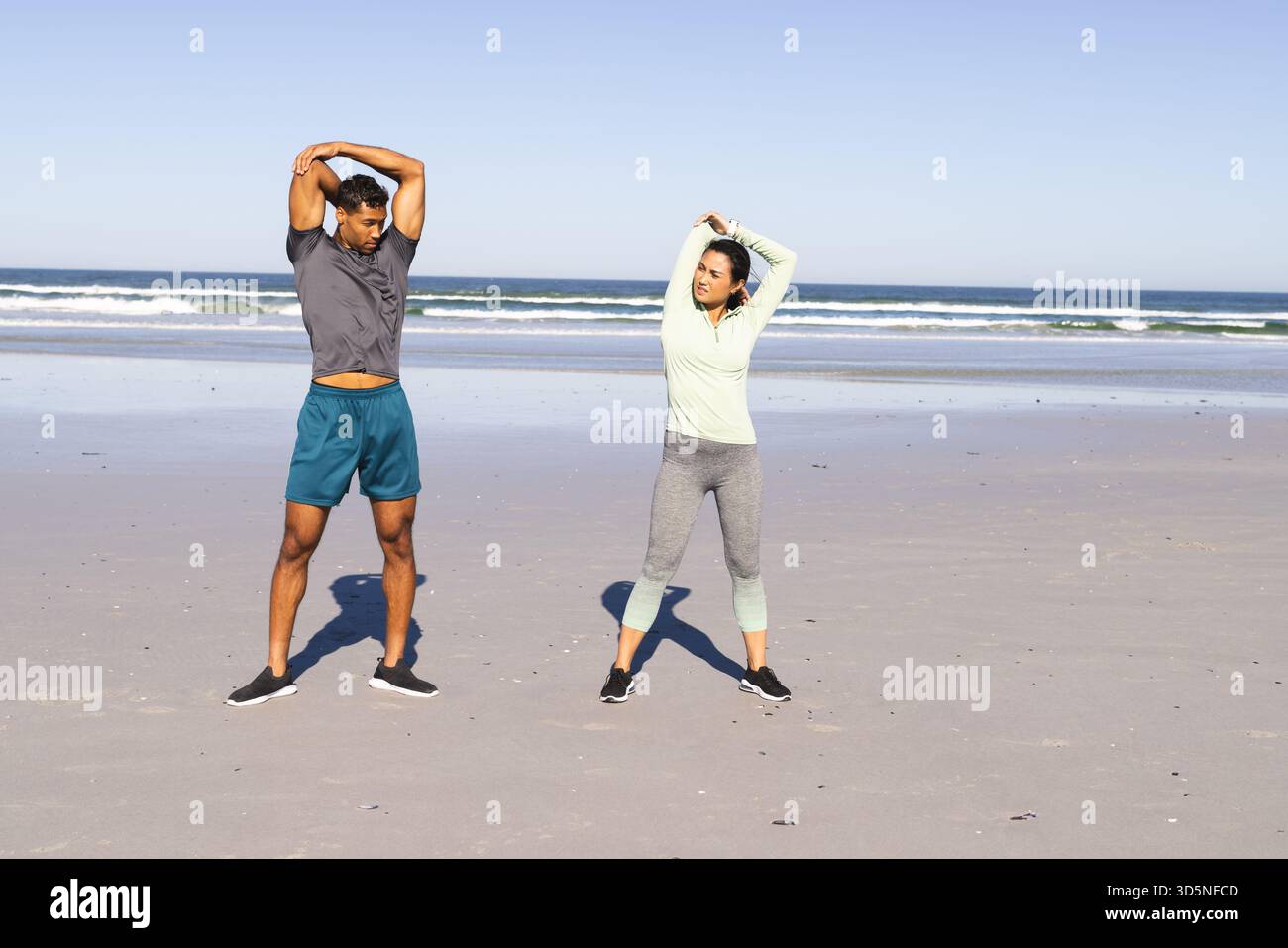 Ci si allunga sulla spiaggia, la coppia fa esercizio mattutino vicino all'oceano, rimanendo attivi Foto Stock
