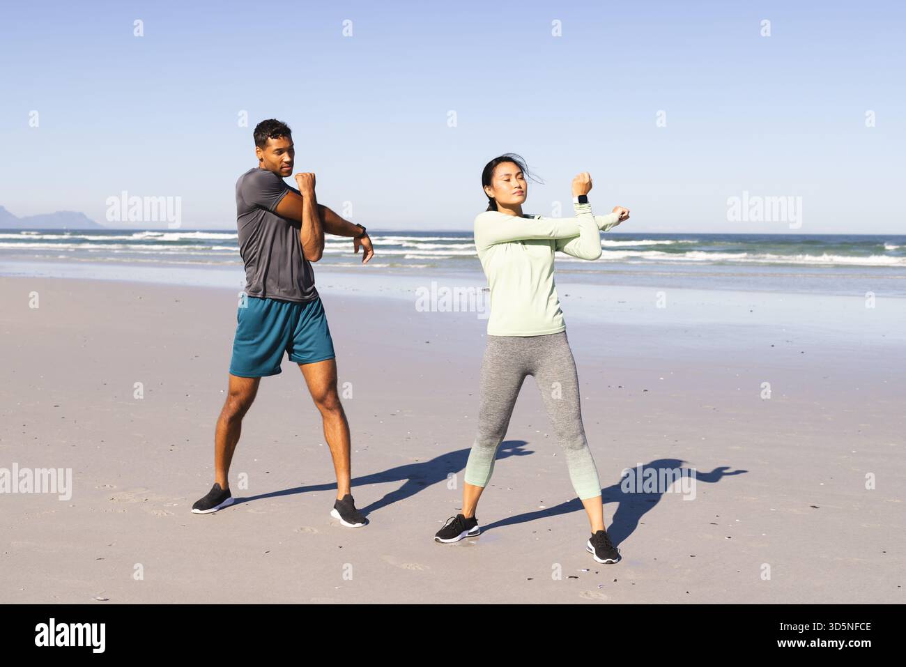 Coppia che si allunga le braccia sulla spiaggia, godendosi l'esercizio mattutino in riva al mare Foto Stock