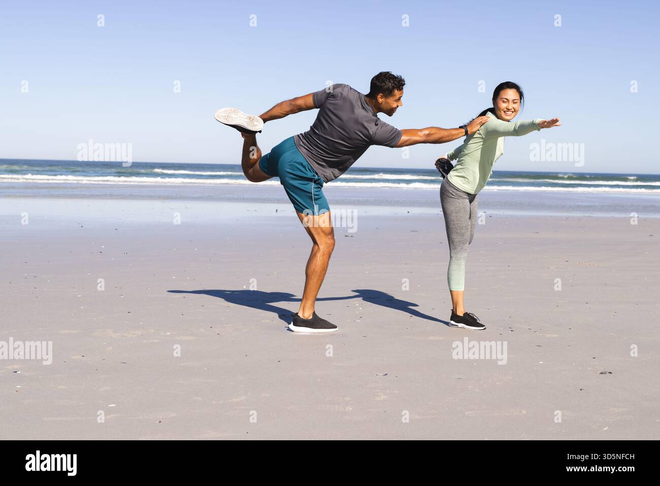 Coppia che si allenano sulla spiaggia, si equilibrano su una gamba, godendosi una giornata di sole Foto Stock