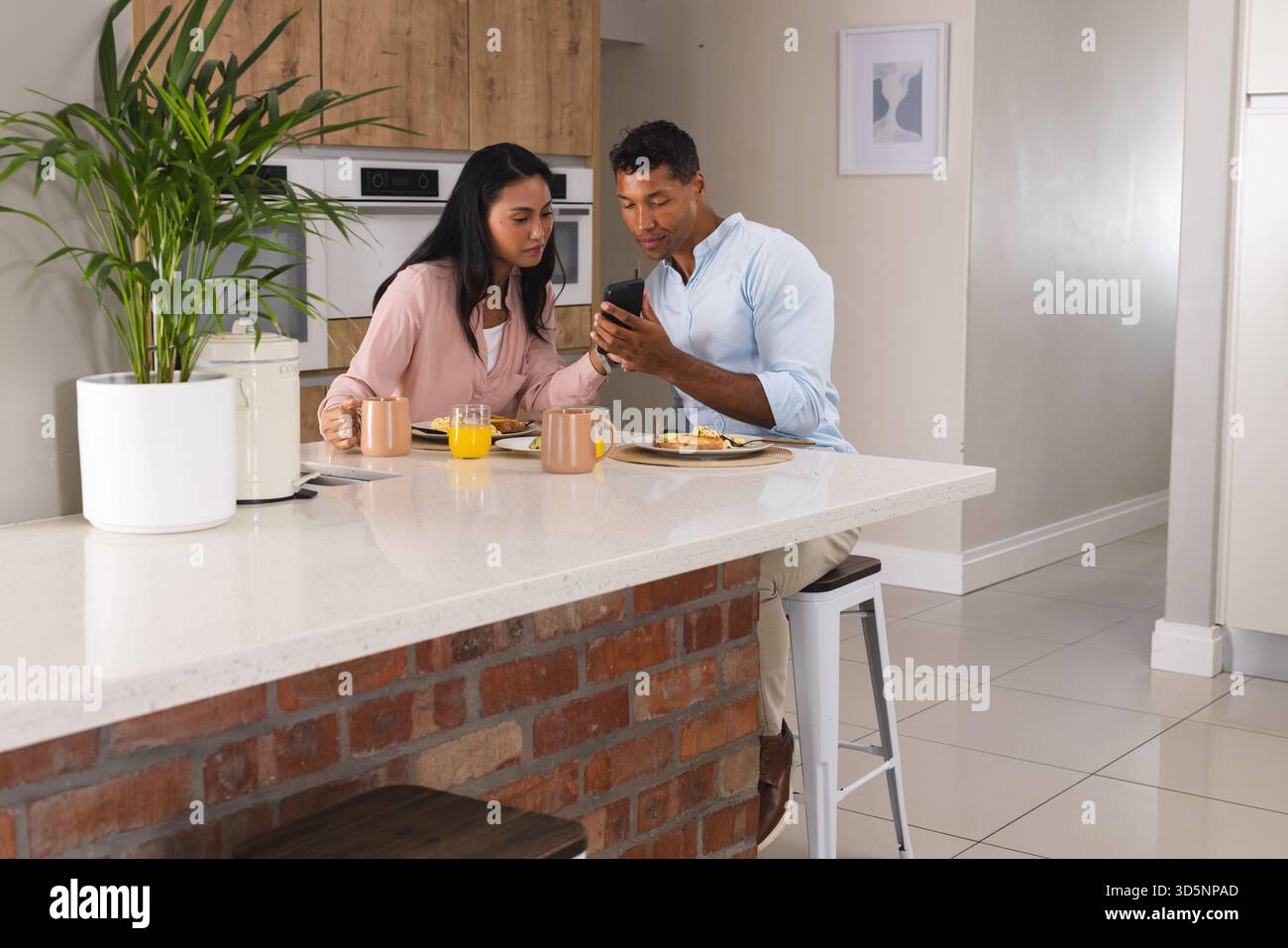 Coppia che fa colazione a casa mentre guarda lo smartphone insieme Foto Stock