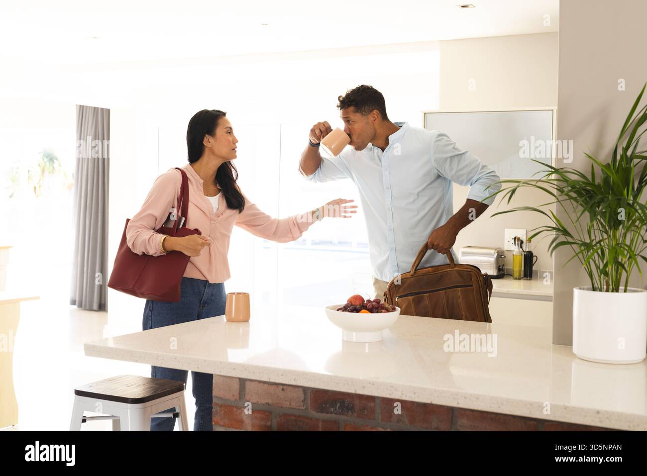 Coppia in cucina, uomo che beve caffè mentre la donna parla, tenendo la borsa Foto Stock