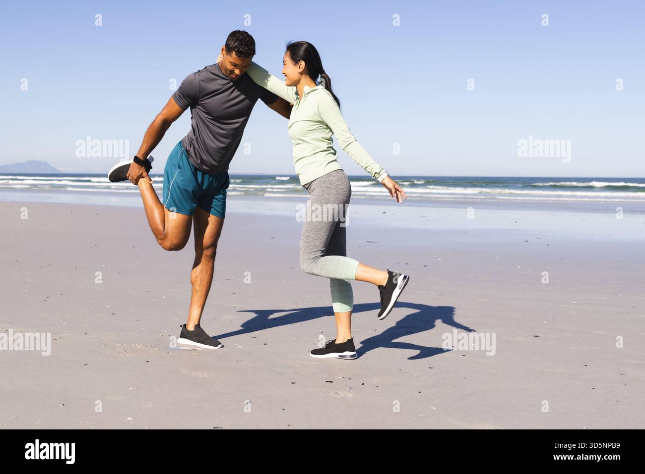 Coppia che si allunga insieme sulla spiaggia, godendosi l'esercizio mattutino in riva al mare Foto Stock
