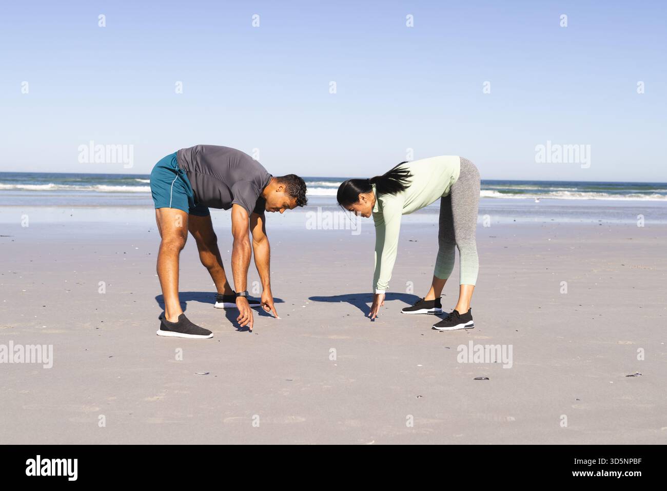 Sulla spiaggia, coppia che si allunga durante l'esercizio mattutino vicino all'oceano, rimanendo attivi Foto Stock