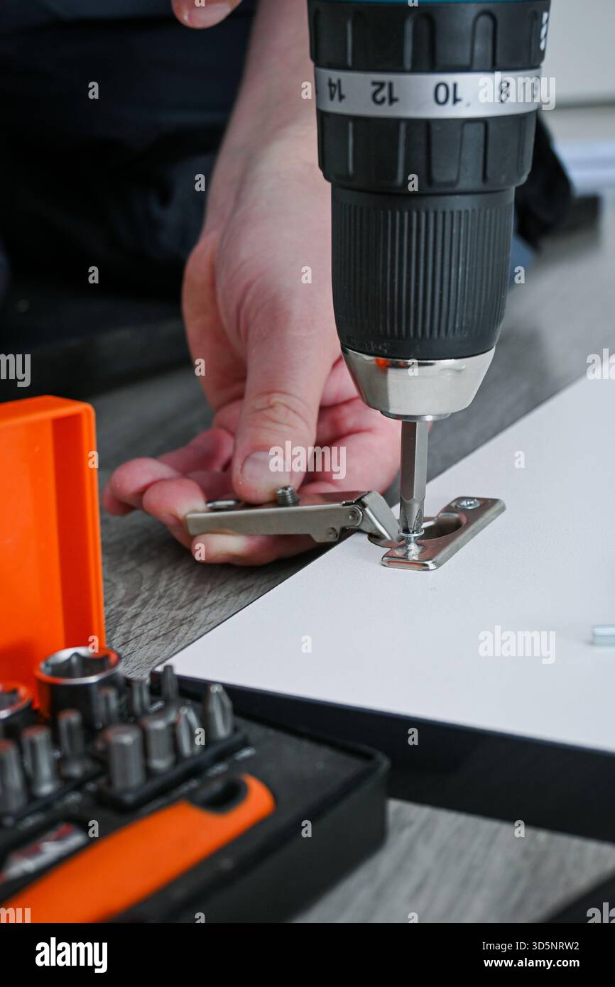 Persona che installa una cerniera di un armadio su mobili utilizzando un cacciavite a batteria. Foto Stock