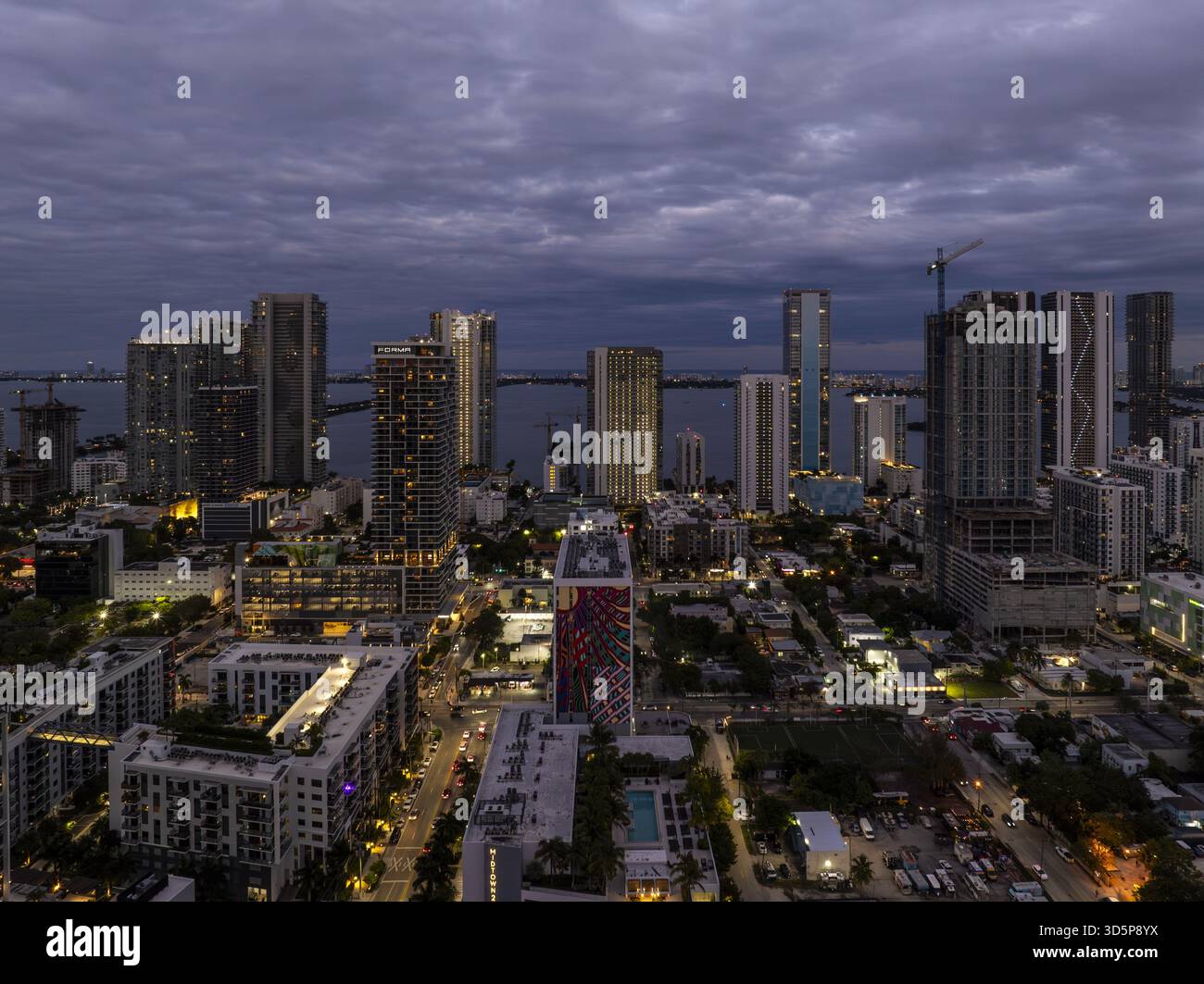 Veduta aerea dei luminosi grattacieli di Edgewater che piergono attraverso il cielo crepuscolo, riflettendo le acque scure della baia, un vivace arazzo urbano che si dispiega Foto Stock