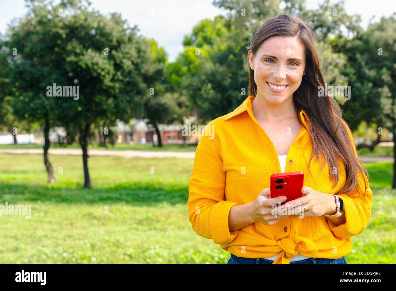 Giovane donna sorridente che usa lo smartphone all'aperto in un parco con spazio fotocopie Foto Stock
