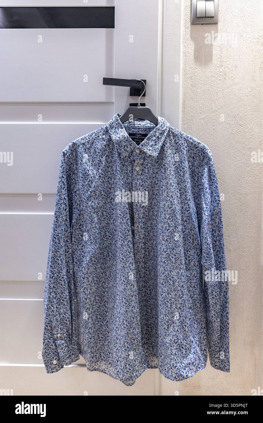 Una camicia blu a maniche lunghe da uomo appesa su un appendiabiti su un pomello della porta su una porta bianca Foto Stock