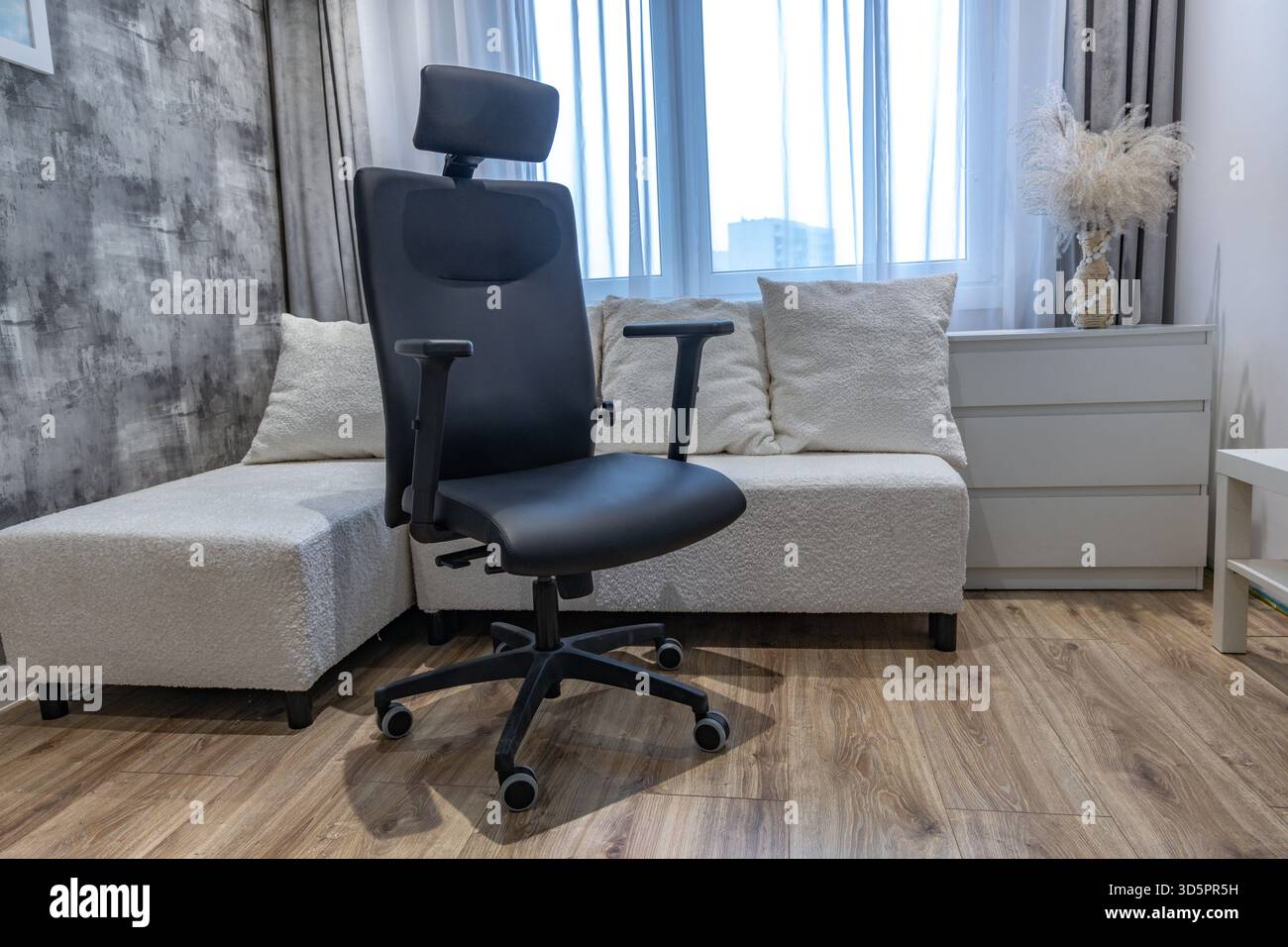 Sedia girevole in pelle nera con altezza regolabile e poggiatesta collocata in un moderno ufficio per uomini d'affari. Foto Stock