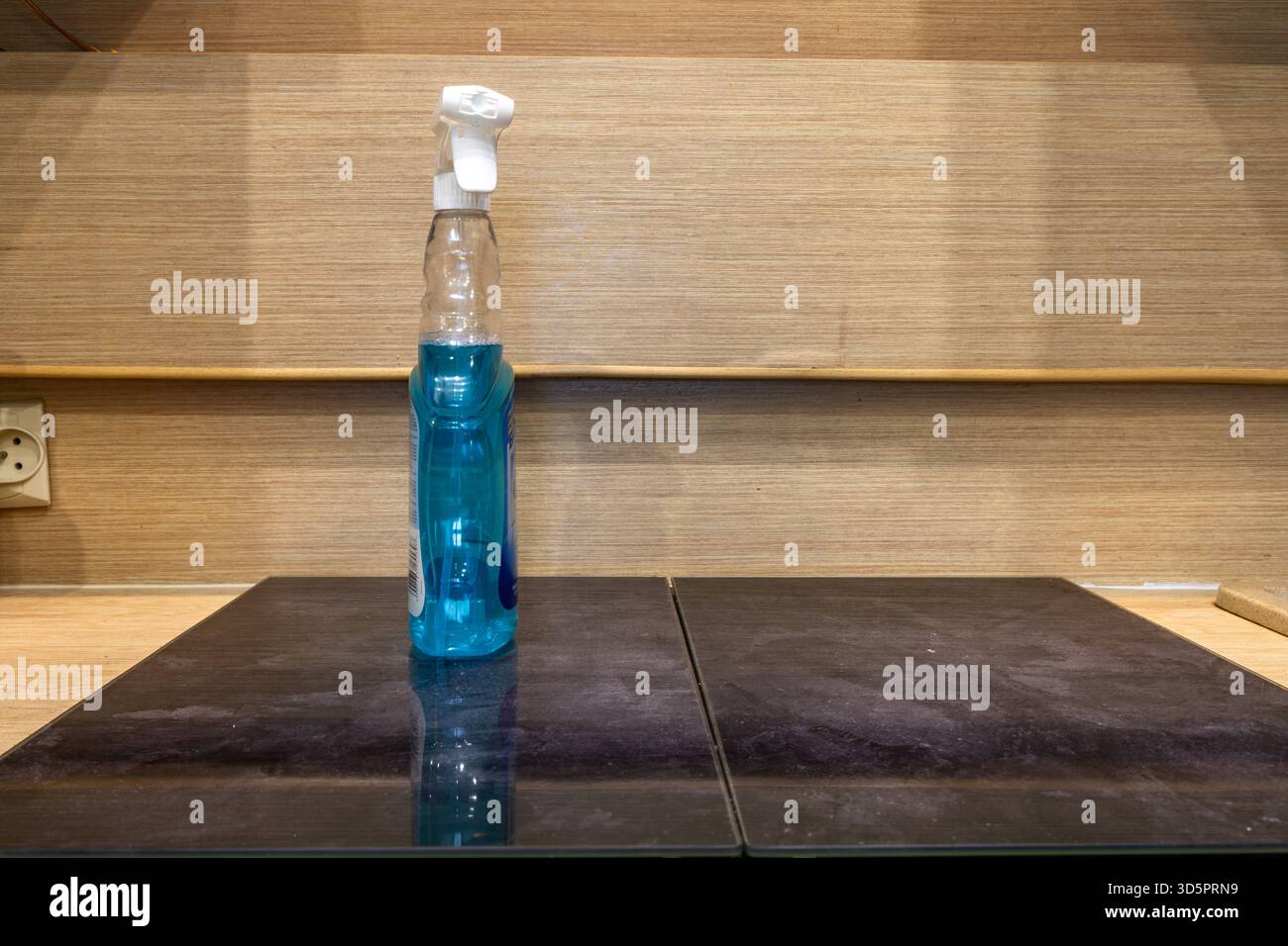 Detergente per vetri blu in una bottiglia trasparente posizionata su un bancone della cucina, per la pulizia in cucina Foto Stock