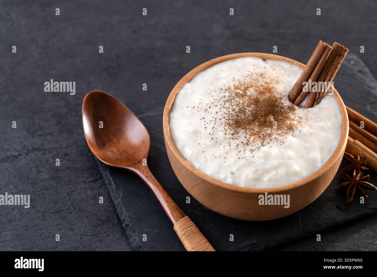 Budino di riso su una ciotola di legno su sfondo di ardesia nera Foto Stock