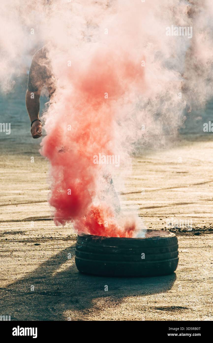Il colorato fumo della torcia del bengala si riversa verso l'alto in caso di evento di auto in movimento, riempiendo l'aria con una fitta foschia intorno a uno pneumatico usato sull'asfalto. Messa a fuoco selettiva. Foto Stock