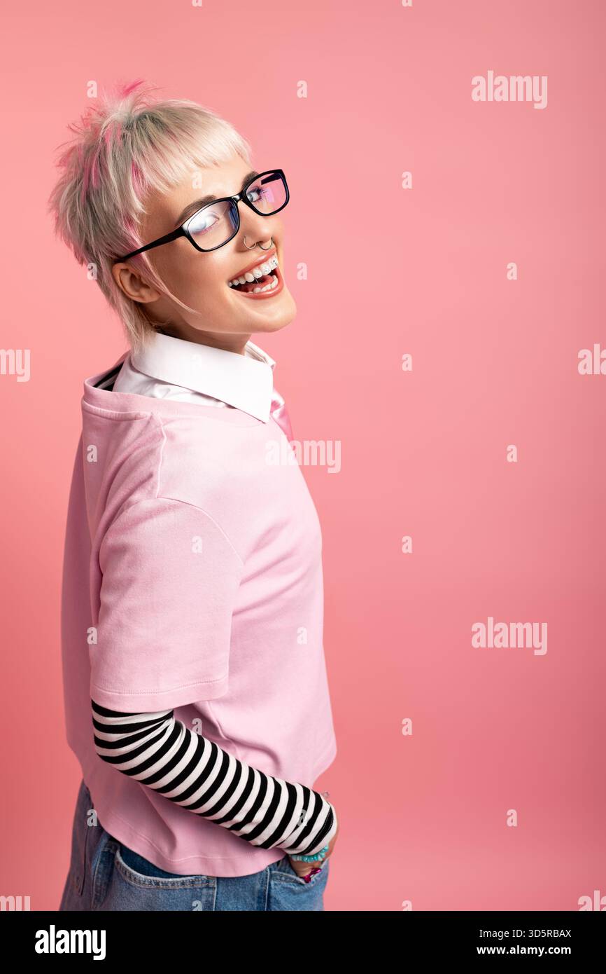 Una giovane donna gioiosa sta in piedi lateralmente, indossando una camicia rosa e maniche a righe, che irradiano felicità. Foto Stock