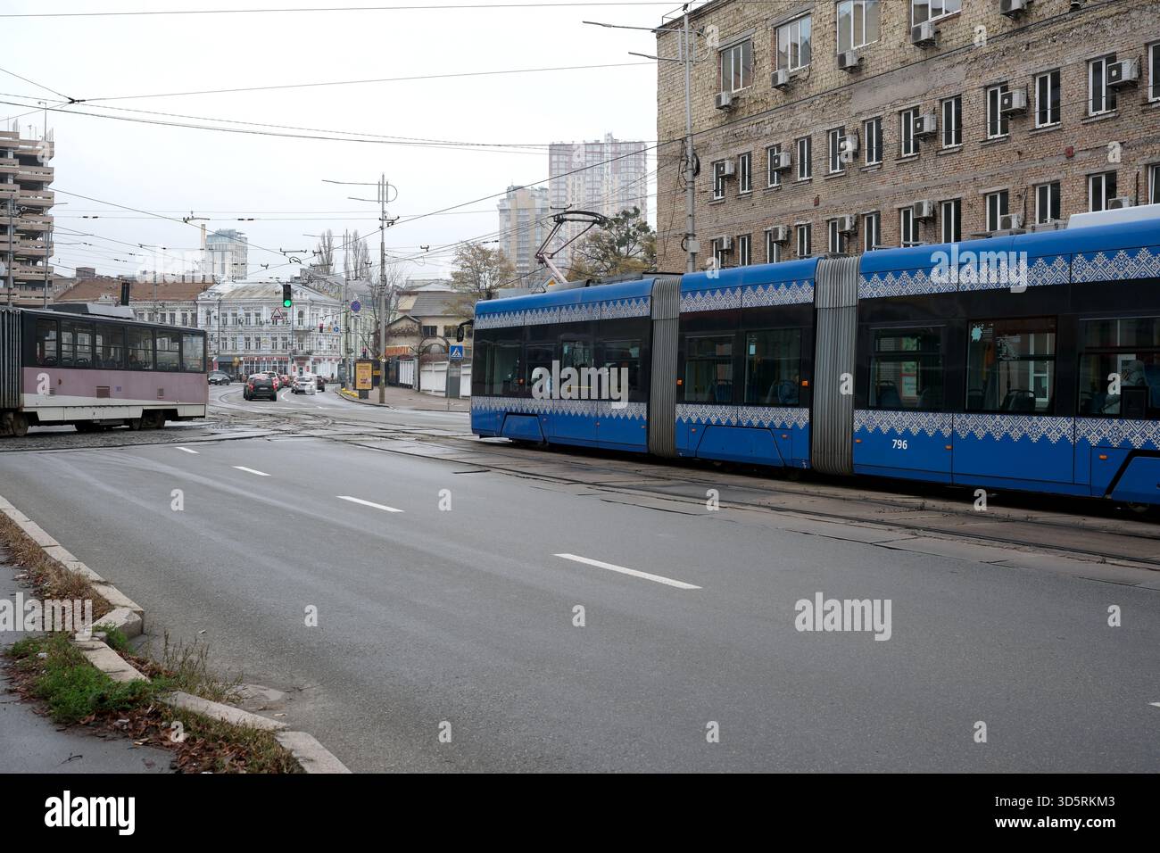 Due tram viaggiano lungo una strada tranquilla a Kiev sotto un cielo grigio autunnale. Foto Stock