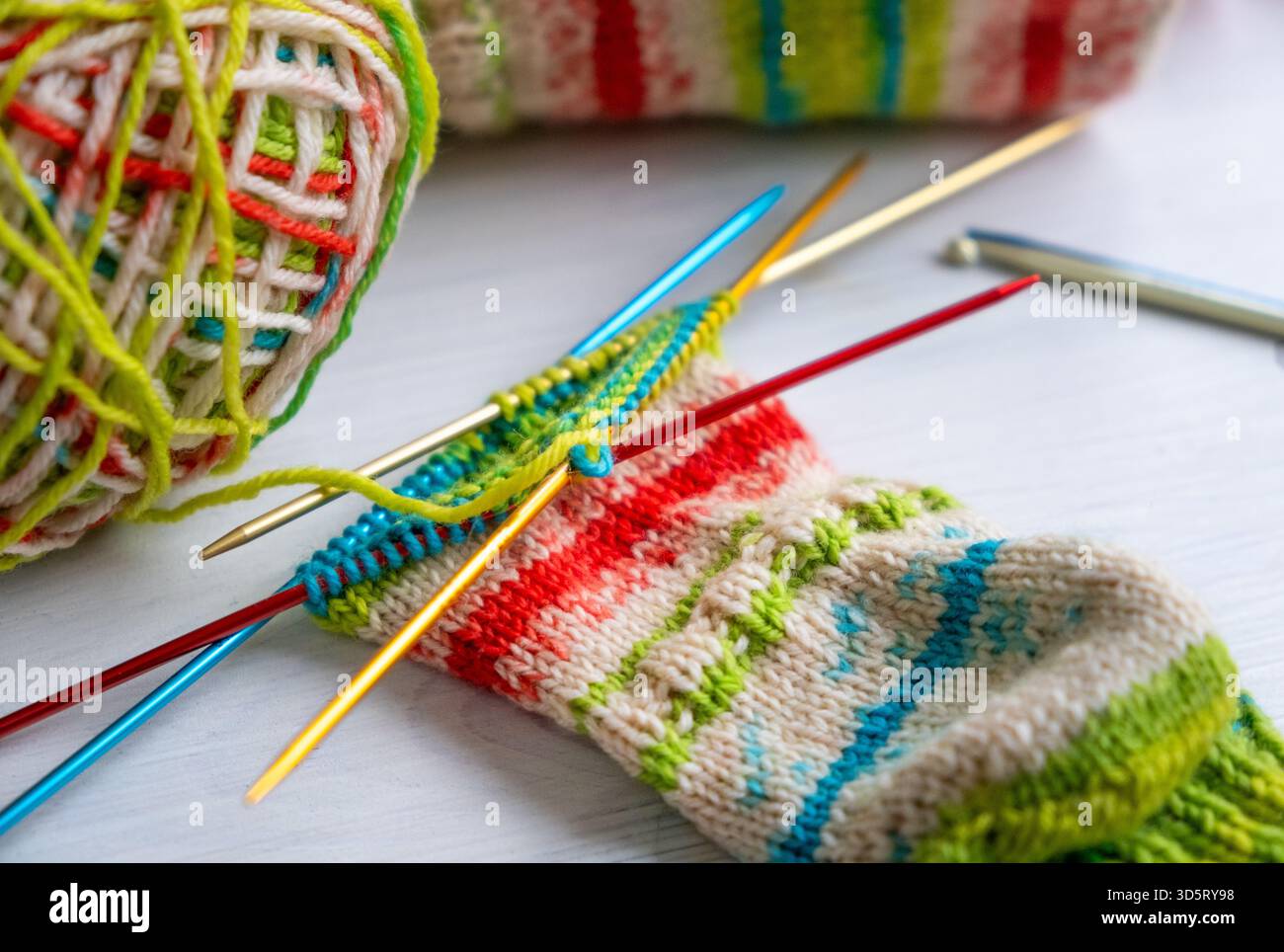 Calzino a maglia colorato in filato di lana multicolore, da vicino con aghi, ideale per hobby, progetti fai da te e temi artigianali Foto Stock