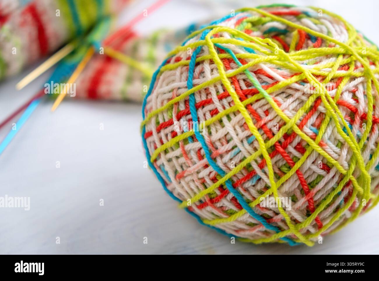 Filato di lana in primo piano con un progetto di maglia sfocato e aghi sullo sfondo, ideale per temi di lavorazione, maglieria, lavorazione della lana e mano Foto Stock