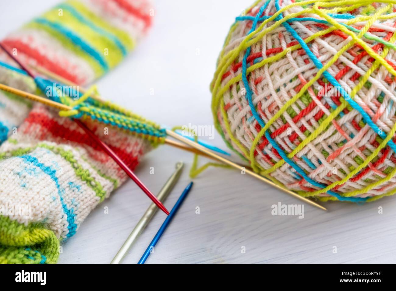 Filati di lana, coloratissimi progetti di maglieria e aghi disposti insieme in primo piano, mostrati in primo piano e ideali per la lavorazione, la lavorazione ad aghi e la mano Foto Stock